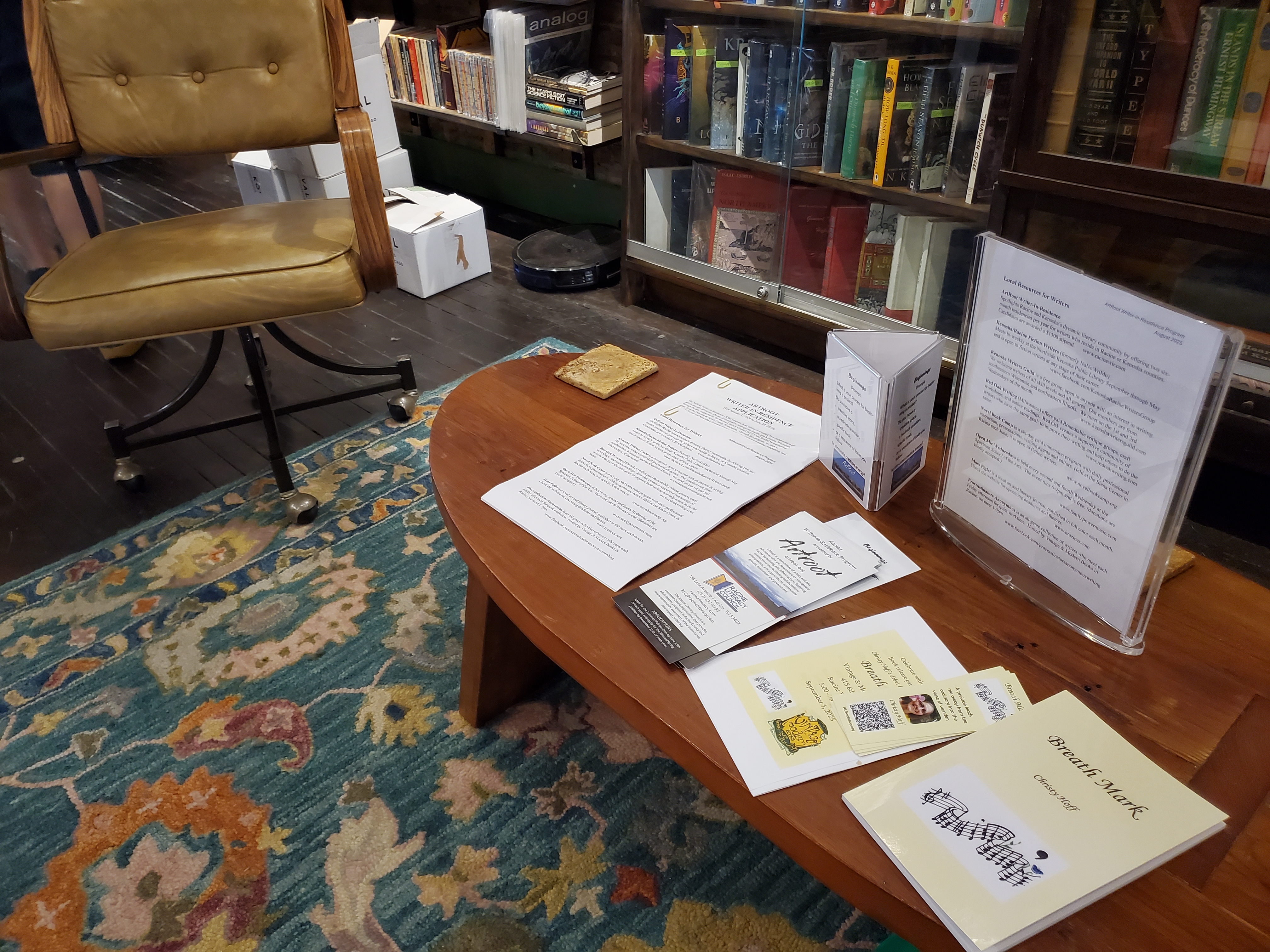 Image shows a table with promotional materials in the foreground with bookshelves in the background.